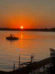 Sunset over a lake with a boat and a wooden dock in the foreground.