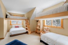 A children's bedroom featuring two bunk beds and a large teddy bear, with natural light filtering through windows.