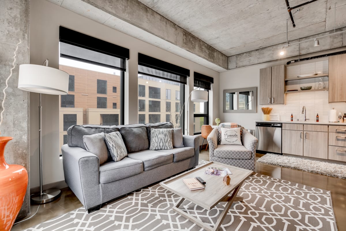 Your modern loft features sleek concrete ceilings, a comfortable gray sectional, and a fully equipped kitchen with city views through expansive windows.