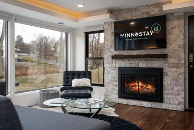 Modern living room with a fireplace, black leather chair, and a television displaying the Minnestay logo.