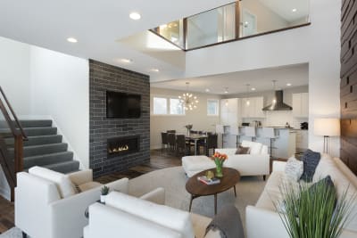 Modern living room with white sofas, a dark stone fireplace, and a dining area in the background.