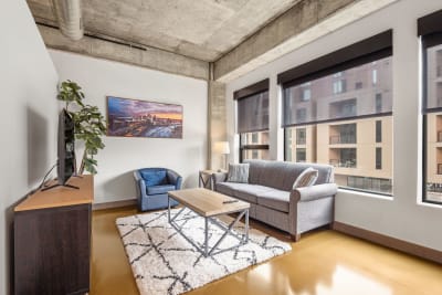 Modern living room featuring a gray sofa, blue accent chair, and large windows, illuminated by natural light.
