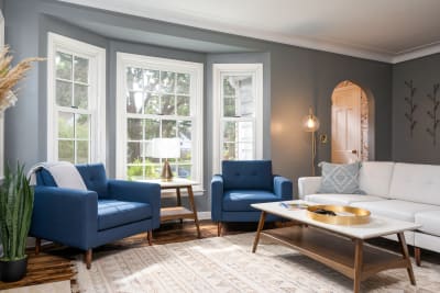 Cozy living room with blue armchairs, a light wood coffee table, and large windows.