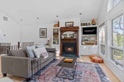 Living room featuring a grey sofa, fireplace, and bright windows, decorated with a rug and cushions.