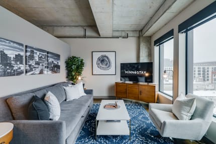 Cozy living room with a gray sofa, stylish decor, and a television displaying the logo 'MINNESTAY'.