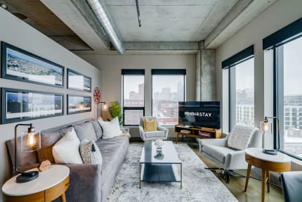 Chic living room in an urban apartment featuring grey sofa, large windows, and city views.