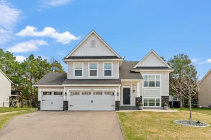 A contemporary two-story house with a black front door and lush green grass.