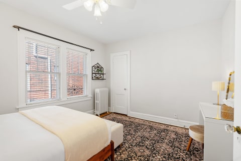 A cozy bedroom with a bed, a desk, and windows letting in natural light.