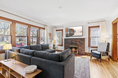 Cozy living room featuring a gray sectional, brick fireplace, and large windows with natural light.