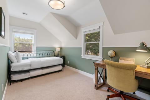 An inviting bedroom with a black daybed, wooden desk, and soft green walls.