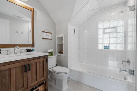 Modern bathroom with white tiles, wooden vanity, and glass block window.