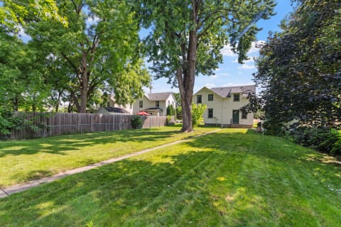 Suburban backyard featuring a well-kept lawn, a path, and two homes surrounded by trees.