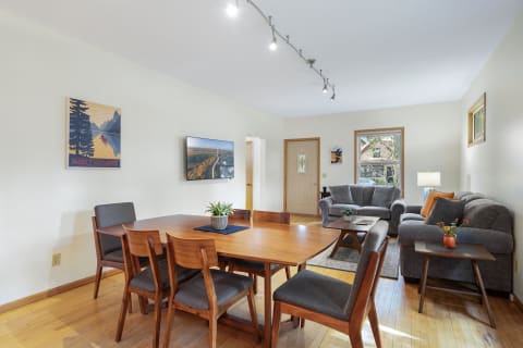 Living and dining area featuring a wooden table, gray chairs, and a comfortable couch, decorated with vibrant wall art.
