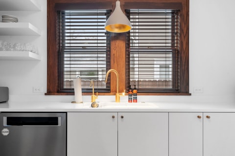 Contemporary kitchen with white countertop, golden faucet, and wooden shelves.