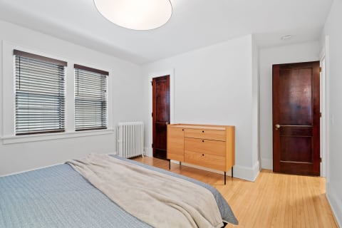 Modern bedroom with large windows, a cozy bed, and a wooden dresser.