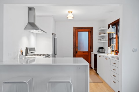 A contemporary kitchen featuring white cabinetry, a stainless steel range, and a wooden door.