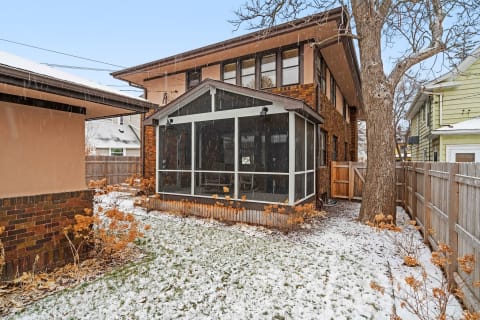 Snowy backyard view with a screened-in porch attached to a brick house.