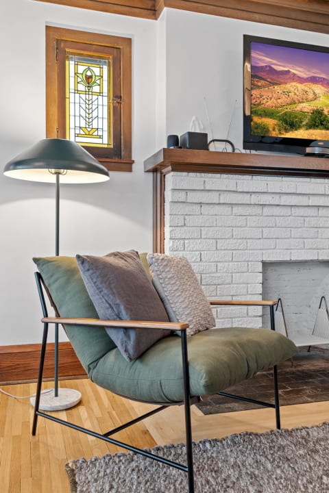 Cozy living room corner featuring a green lounge chair, modern floor lamp, stained glass window, and white brick fireplace.