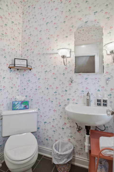 Charming powder room featuring floral wallpaper, toilet, sink, and modern amenities.