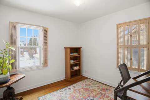 A reading nook with a wooden bookshelf, a cozy rug, and a window with wooden shutters.