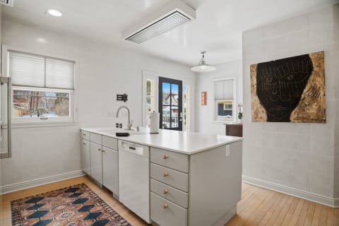 Modern kitchen with white countertops, an artistic wall piece, and large windows letting in natural light.