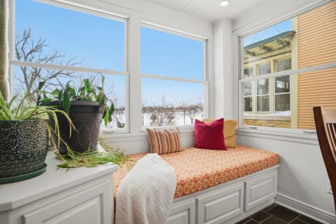 Sunny window seat with orange patterned cushions and potted plants, featuring winter scenery outside.