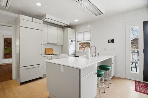 Modern kitchen with white cabinetry, breakfast island, green stools, and hardwood flooring.