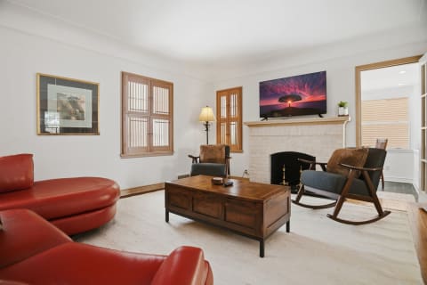 A cozy living room with bright red leather seating, a wooden coffee table, and a fireplace with a TV mounted above it.