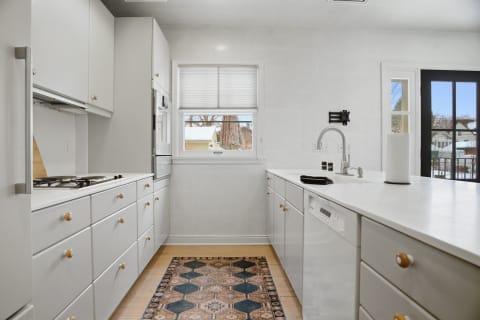 A modern kitchen with white cabinets and a black-framed door leading outside.
