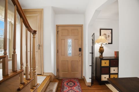 A warmly lit foyer featuring a wooden door, staircase, and decorative furnishings.