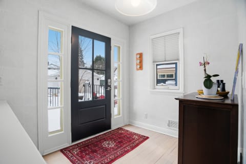 A bright entryway with a black door, a red rug, and natural light streaming in from windows.