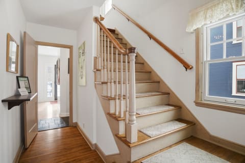 Inviting hallway with a wooden staircase and vibrant artworks on walls.