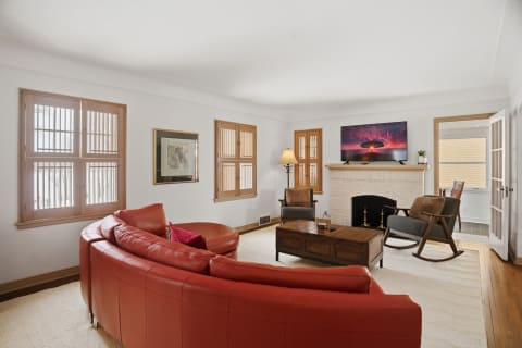Spacious living room with red leather seating, television above a stone fireplace, and wooden windows.