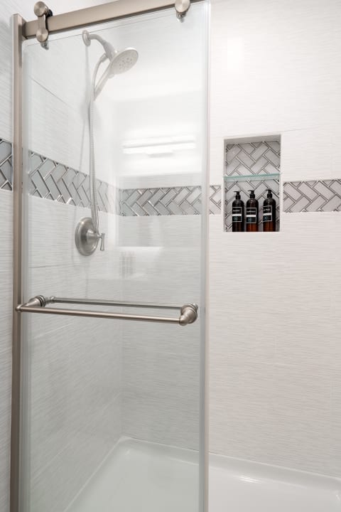 Modern shower with glass door, textured white tiles, and herringbone patterned accents.