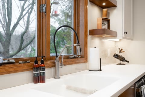 A kitchen sink with modern faucet, hand soap, lotion bottles, and a view of trees outside.