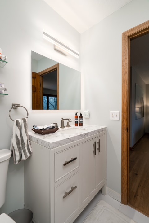 A modern bathroom with a white marble countertop, gray walls, and wooden accents.