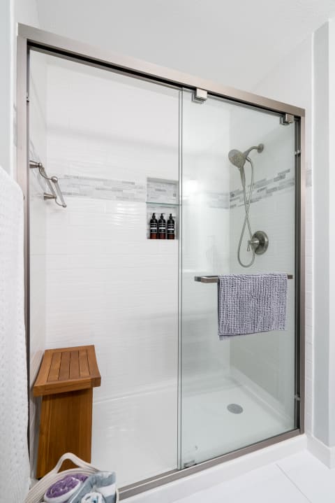 Contemporary shower featuring glass doors, a wooden bench, and decorative tiles.