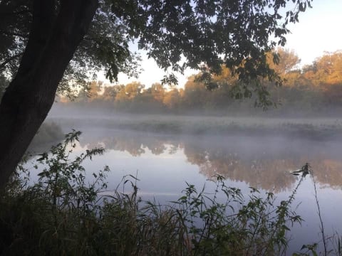 A peaceful river scene at dawn with mist rising off the water and autumn trees in the background.