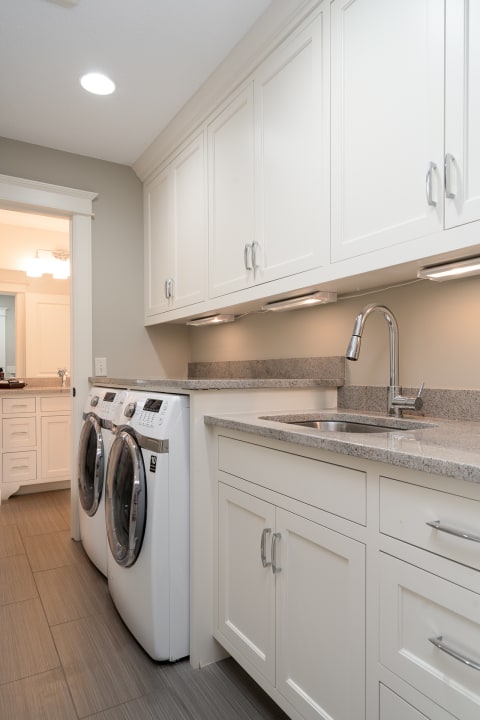Modern laundry room featuring white cabinetry and front-load washing machines.