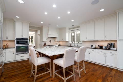 A modern kitchen featuring white cabinets, a granite island, and hardwood floors.