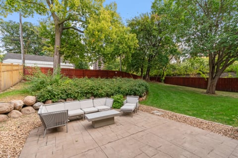 Outdoor patio with gray furniture surrounded by trees and a wooden fence.