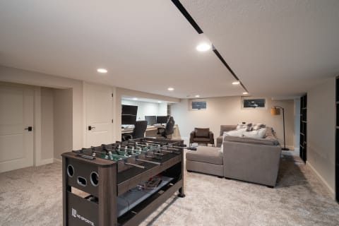 Modern basement with foosball table, sectional sofa, and desk area.