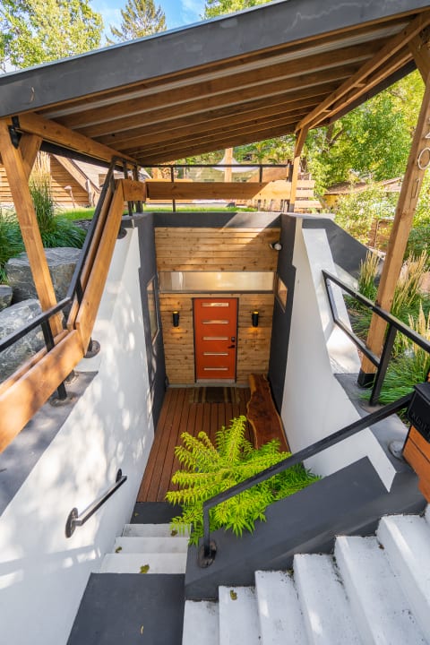 Modern home entrance featuring an orange door and steps surrounded by greenery.