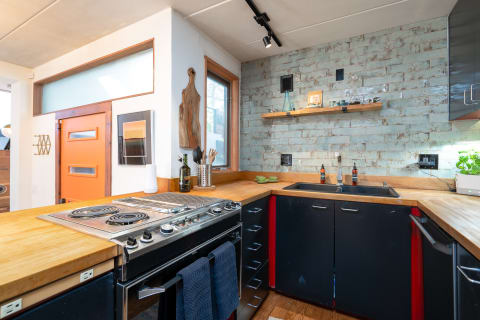 A stylish kitchen featuring a black stove, teal brick wall, and an orange door.