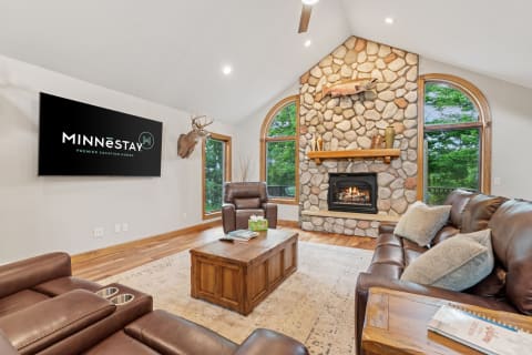 Living room featuring a stone fireplace, leather couches, and a flat-screen TV with vacation rental branding.