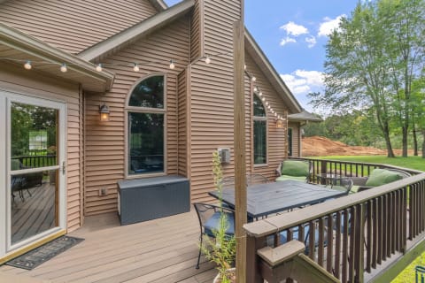 Outdoor deck with seating and lights attached to a wooden house, featuring trees in the background.