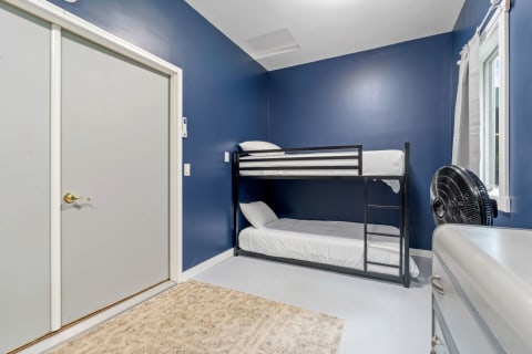 A small room with a bunk bed, navy blue walls, and a window with curtains.