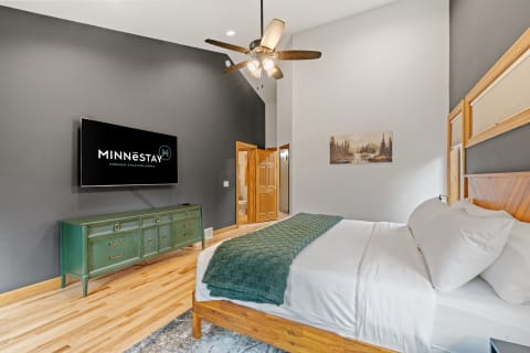 Modern bedroom with a green sideboard, wall-mounted TV, and a bed with white linens and a green blanket.