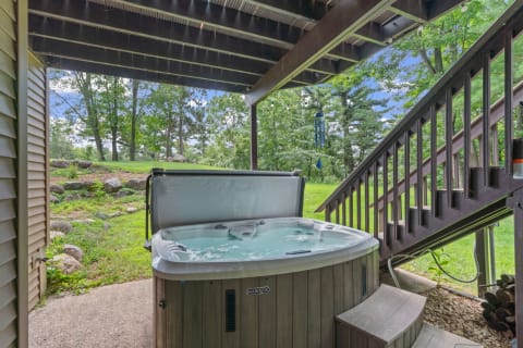 Hot tub on a patio with a view of green landscape and wooden stairs.