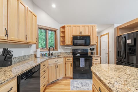 Modern kitchen featuring light wood cabinetry and black appliances with a natural view.